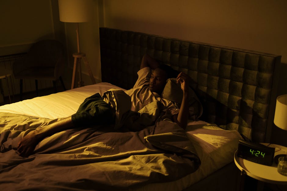 A restless man lying awake on his bed in a dimly lit bedroom at night.