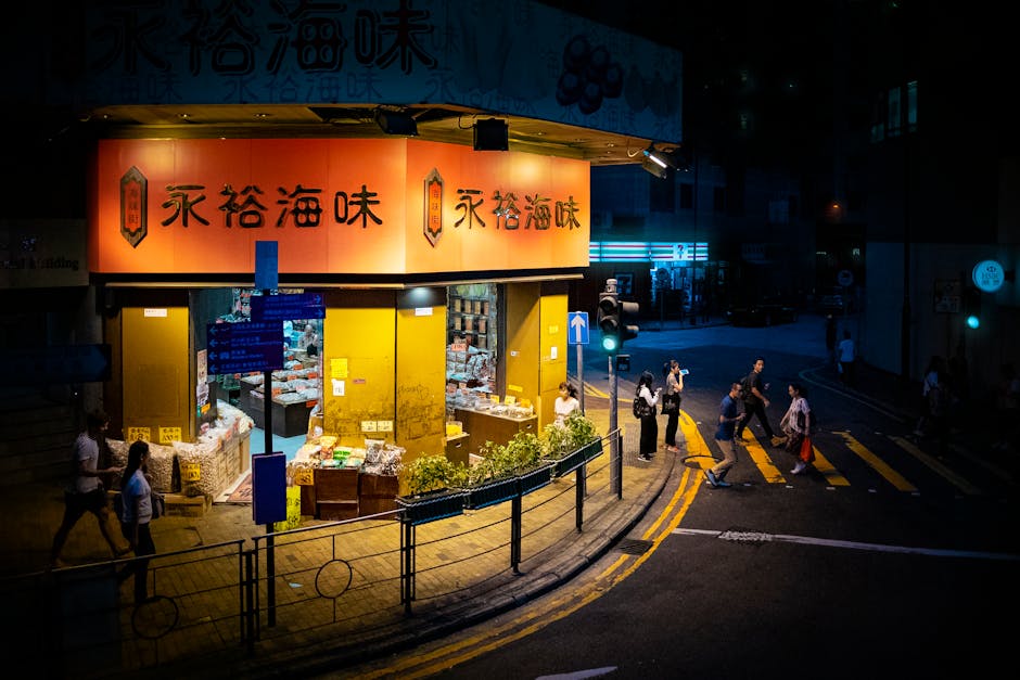 Illuminated Hong Kong storefront by night with pedestrians crossing, capturing vibrant urban life.