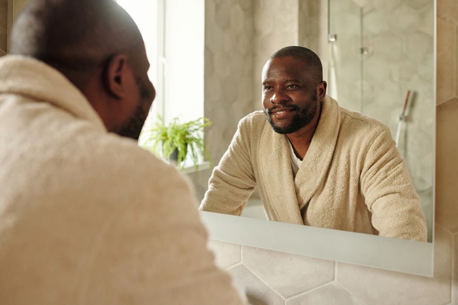 African American man smiling at his reflection in the bathroom mirror, wearing a bathrobe.