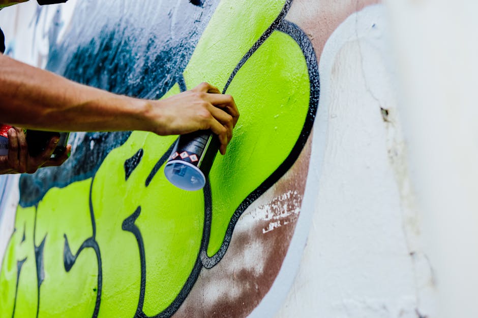 Close-up of a vibrant street artist spray-painting a colorful graffiti mural outdoors.