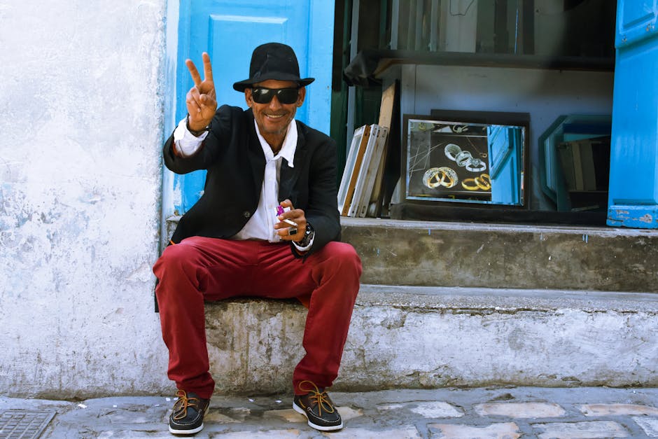Fashionable man with sunglasses and peace sign sitting on Tunis sidewalk.