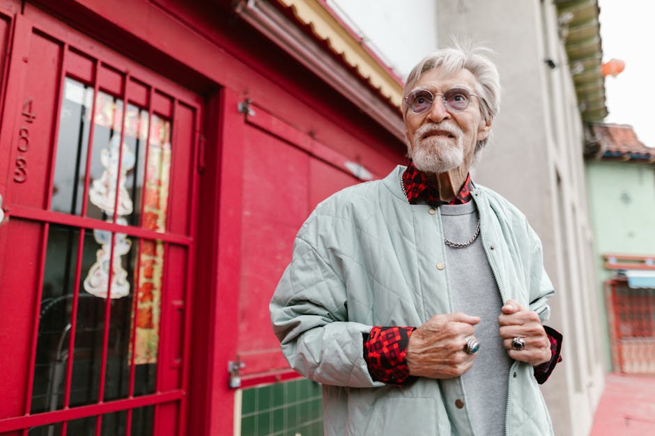 An elderly man in a fashionable outfit poses confidently in a vibrant city environment.
