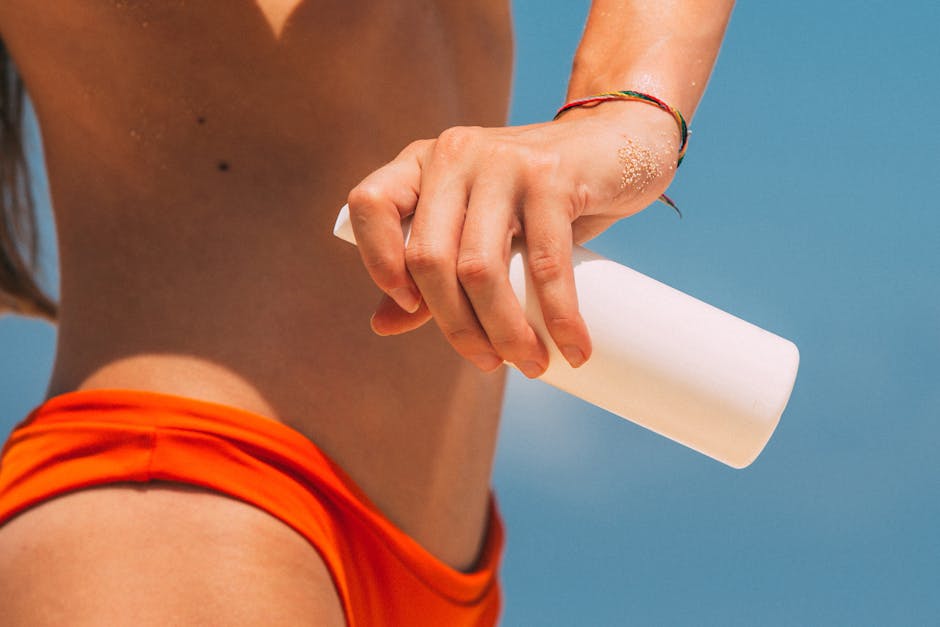 A close-up of a woman applying sunscreen from a white bottle at the beach.