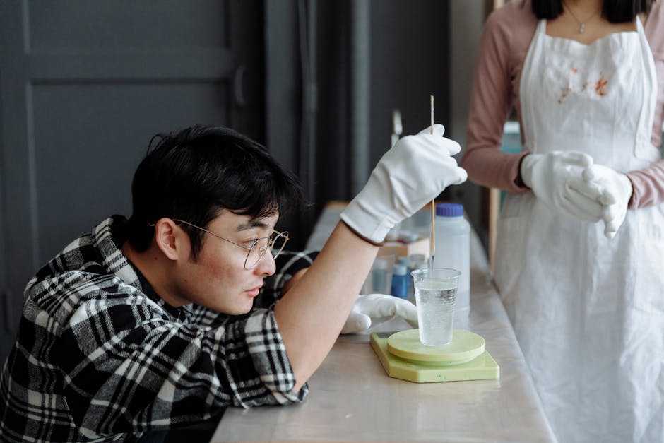 Asian man wearing gloves carefully mixes resin in a plastic cup inside a workshop.
