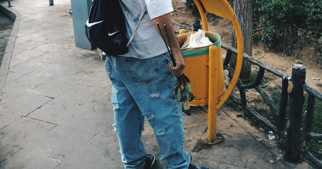 A person stands near a trash can outdoors.