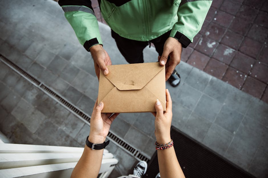 Close-up of hands exchanging a brown envelope outdoors on a pavement scene.