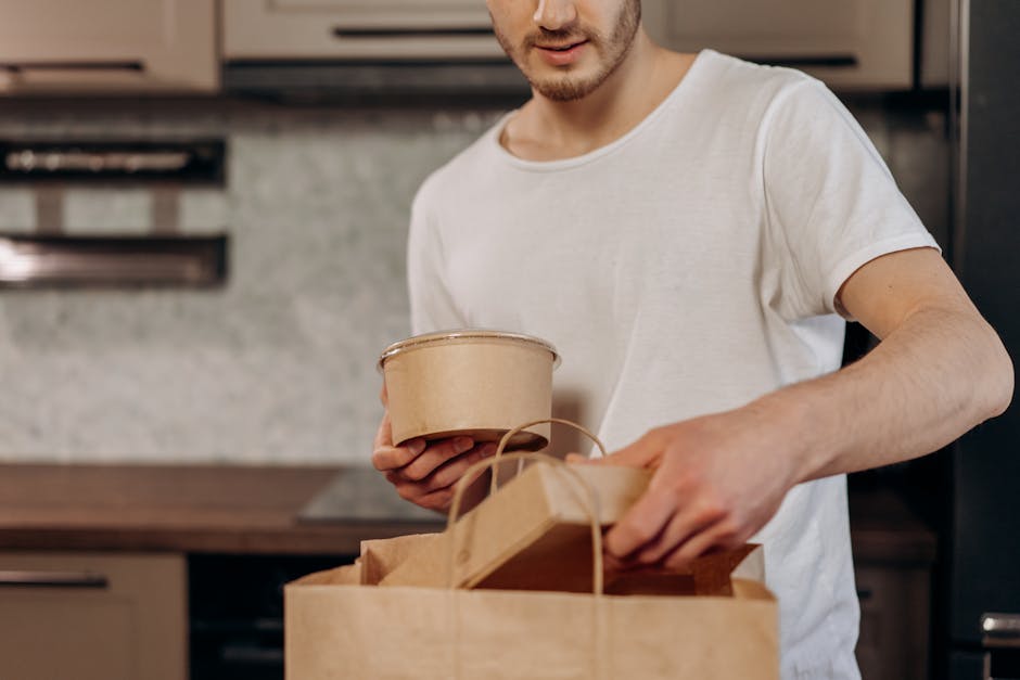 Man placing takeout containers into paper bag in kitchen setting.