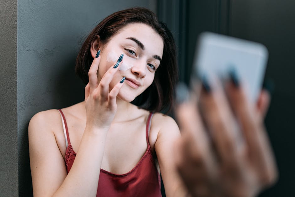 Young Caucasian woman applying moisturizer while smiling in front of a mirror indoors.