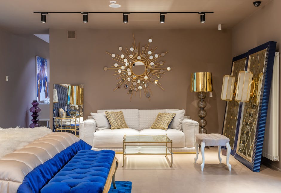 Comfortable white sofa with cushions near table at wall with decorative elements in spacious apartment with bed near blue bench