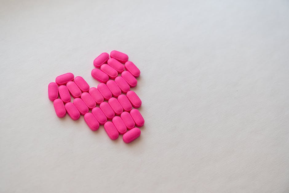 Creative arrangement of pink pills in a heart shape on a white background, symbolizing health and love.