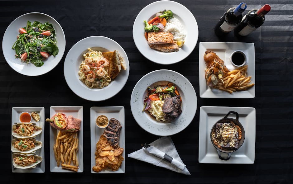 Top view of elegantly plated restaurant dishes paired with wine bottles, showcasing diverse cuisine.