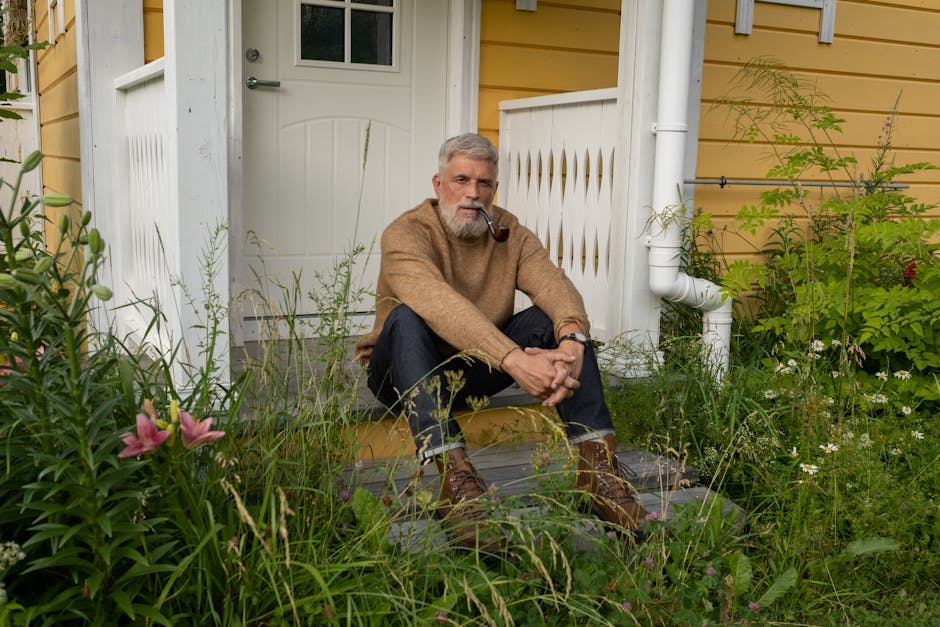 Senior man with gray hair sitting on a porch, enjoying a calm moment with a pipe.