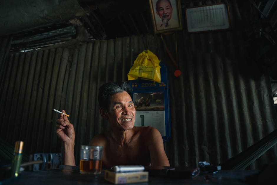 Smiling middle-aged man sitting indoors, holding a cigarette, creating a relaxed and casual atmosphere.