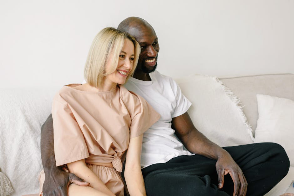 Smiling interracial couple sitting on a cozy couch, enjoying their time together at home.