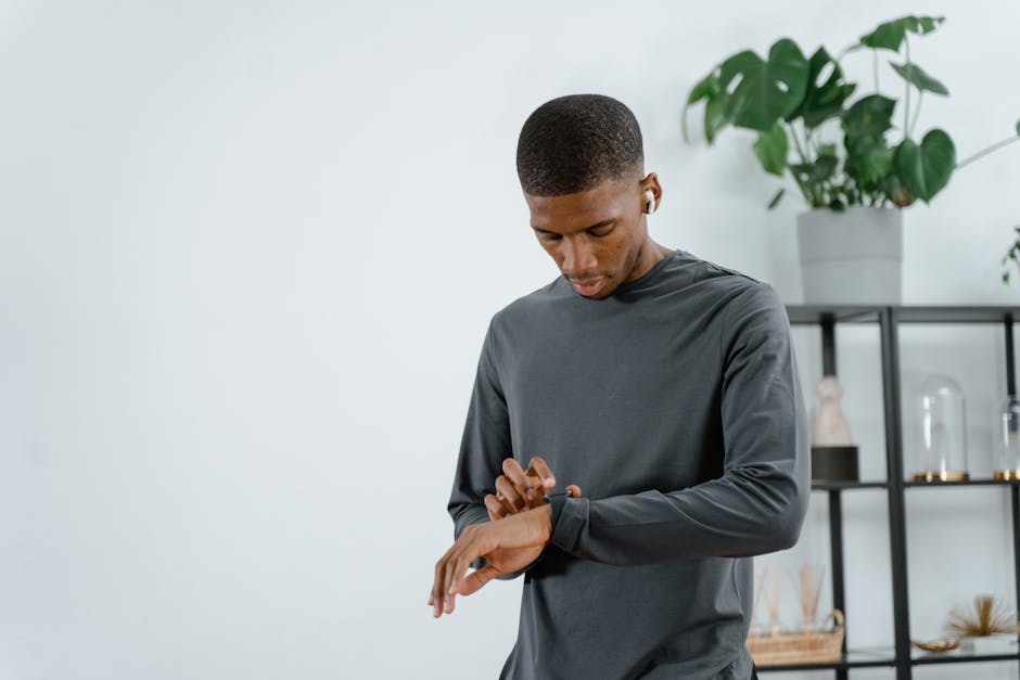 A man in a gray sweatshirt checks his smartwatch while standing in a stylish indoor setting with plants.