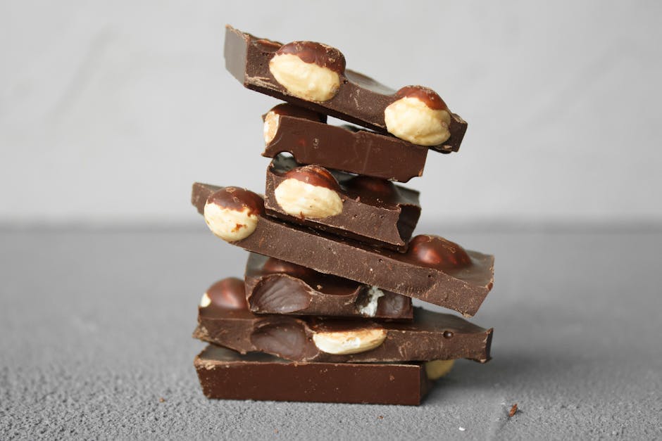 A stack of dark chocolate bars filled with whole nuts on a textured gray background.
