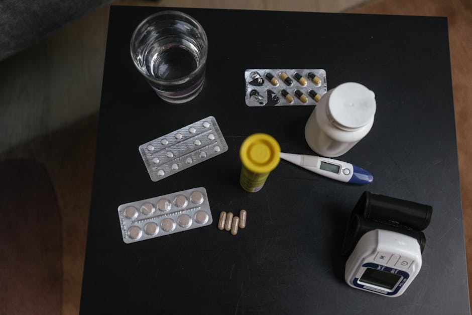Top view of various medications, tablets, and medical devices on a table with a glass of water.