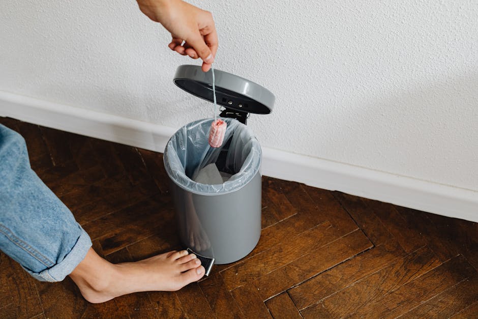 A person disposing a tampon in a trash bin with a foot pedal inside a home setting.