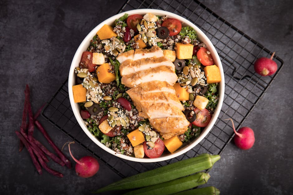 A vibrant bowl of grilled chicken salad with quinoa, fresh vegetables, and seeds.